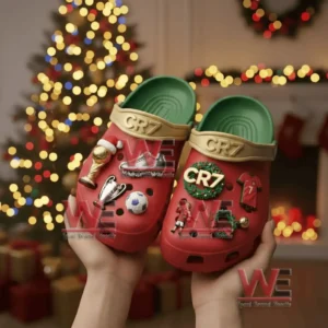 Hands presenting red CR7 clogs decorated with football and Christmas themed charms before a lit tree!