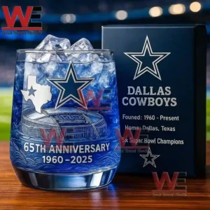 A blue Dallas Cowboys sixty fifth anniversary glass with ice standing beside a team themed box on a wooden surface!
