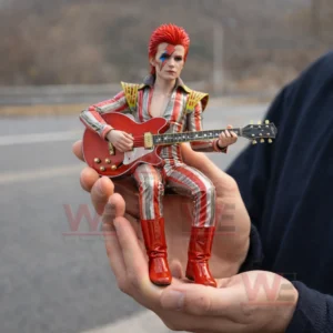 David Bowie Stardust Car Display Resin Figure Doll 3 Small resin figure of a red haired glam rock musician with face paint holding a red electric guitar while being held in two hands outdoors!