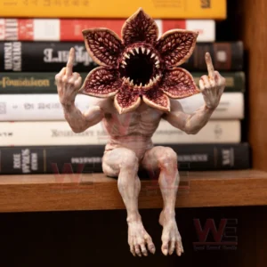 A horror creature figurine with a flower shaped mouth sitting on a shelf in front of books with both hands raised!