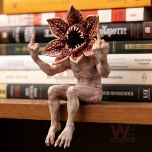 A collectible monster figurine with a flower shaped mouth sitting on a shelf in front of books raising both hands!