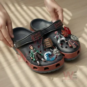 Demon Slayer themed clogs with black and red colors decorated with anime character charms being held by hands on a wooden floor!