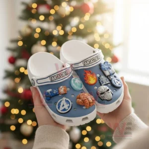 Blue and white clogs with superhero themed charms held in front of a Christmas tree!