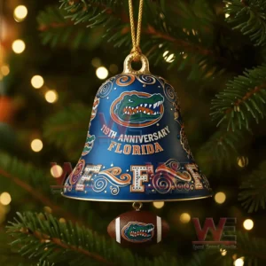 A close up view of a Florida Gators anniversary bell ornament featuring ornate designs team logos and a football charm hanging beneath it against soft glowing festive lights!