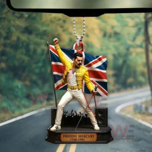 Car hanging ornament showing a Freddie Mercury figure in a yellow jacket and white pants standing in front of a Union Jack flag with a microphone stand on a small base.