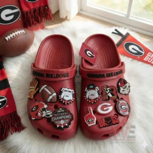 A pair of red Georgia Bulldogs clogs adorned with numerous themed charms placed among team decorations and football items!