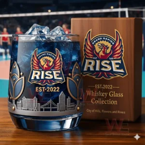 A close view of a Grand Rapids Rise whiskey glass containing a blue drink and ice displayed beside its wooden box featuring phoenix imagery and skyline engravings!