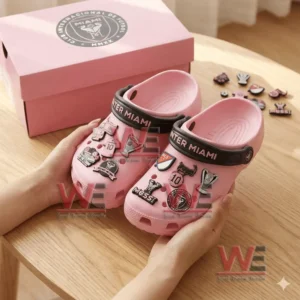 Pink Inter Miami clogs with multiple team and player charms held above a pink branded box.