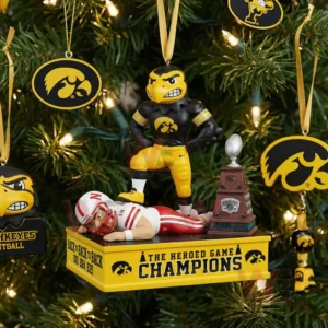 Iowa Hawkeyes mascot standing on a rival with a trophy on a yellow Heroes Game champions ornament hanging on a Christmas tree.