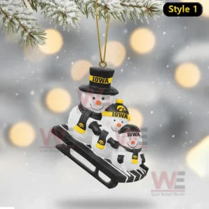 Three Iowa themed snowmen on a sled ornament hanging from a snowy branch with blurred winter lights behind!