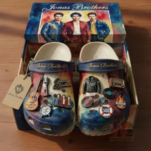 Open shoebox showing Jonas Brothers themed clogs with navy straps and gold lettering, decorated with guitar microphone vinyl and radio charms with matching band artwork on the lid.
