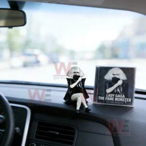 Lady Gaga figurine sitting on a car dashboard next to The Fame Monster album case with a bright outdoor view!