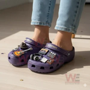 Feet wearing purple Leon Thomas clogs decorated with music and film themed charms including a guitar headphones a hat and a clapper.