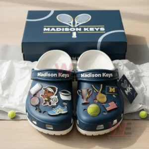 A pair of blue tennis themed clogs shown in front of a branded box with multiple sporty charms attached to the front area!