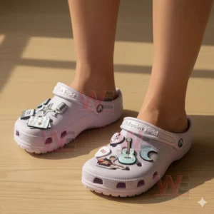Feet wearing light pink clogs adorned with multiple music inspired charms in a bright indoor setting!