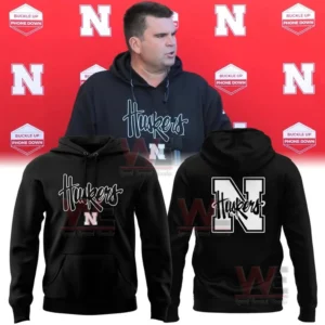 Man wearing a black Husker hoodie in front of a red backdrop with product mockups showing the hoodie front and back designs!