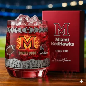 A close view of a Miami RedHawks whiskey glass filled with a red drink and ice displayed beside its red box featuring team branding and forest engravings!