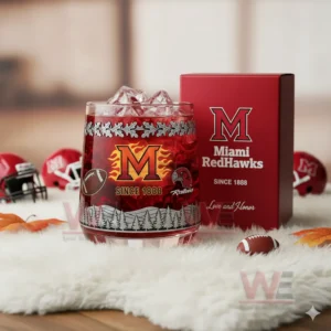 A detailed image of a Miami RedHawks glass containing a red drink with ice displayed beside its branded red box on a soft white surface with sports accessories nearby!