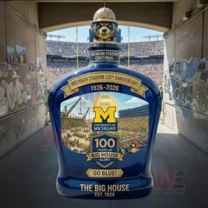 Blue Michigan Stadium centennial decanter with a wolverine hard hat topper and a one hundred years Big House label shown in a stadium tunnel opening to a crowded field.