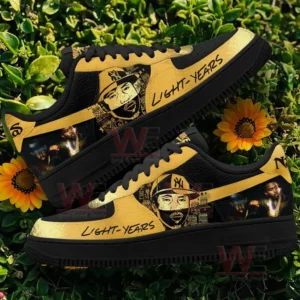 Nas Light Years themed gold and black low top sneakers with portrait artwork displayed on greenery with yellow flowers!