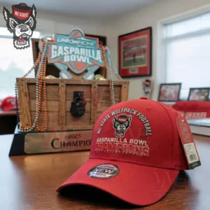 Red NC State Wolfpack Gasparilla Bowl Champions cap positioned on a table with a trophy and sports decorations in the background!