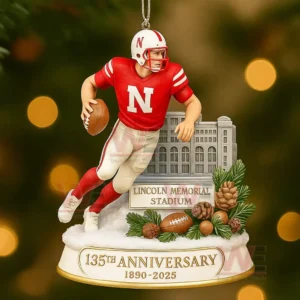 Ornament of a red uniformed football player holding a ball positioned before a small stadium replica with anniversary text displayed below