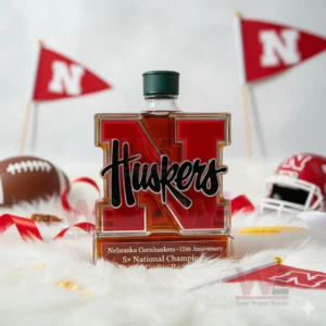 Nebraska Cornhuskers 5x National Champions Go Big Red Whiskey Bottle 7 A red N Huskers bottle displayed on white fur with football equipment and team flags in the background.