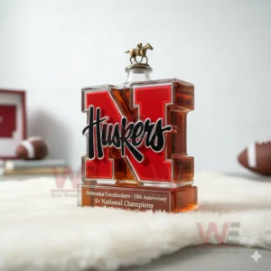 Nebraska Cornhuskers 5x National Champions Go Big Red Whiskey Bottle 8 A red N Huskers bottle with a horse rider cap placed on a white fur mat with football props nearby.