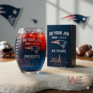 New England Patriots 65th Anniversary Football Whiskey Glass 4 A football shaped glass with a two tone red and blue drink next to an anniversary box in a room decorated with team symbols and football items!