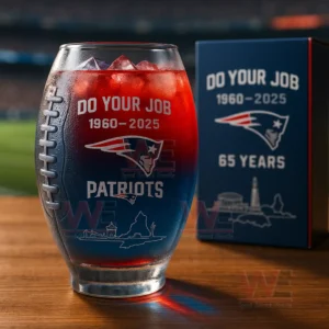 A football shaped glass with engraved team graphics holding a red and blue drink next to a decorative box on a table!