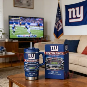 Blue New York Giants tumbler with straw and matching box on a wooden coffee table with a television showing a football game and Giants wall banner in the background.