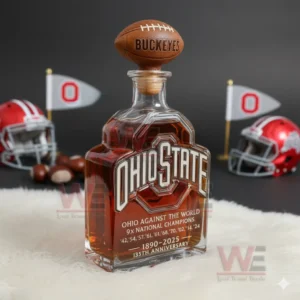 An Ohio State anniversary bottle with a football cap on white fur with helmets flags and buckeye nuts nearby.
