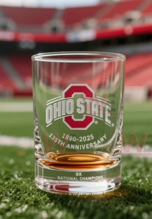 Ohio State themed glass with amber liquid on football field turf with stadium seats softly out of focus!