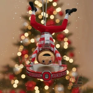 An ornament of Brutus Buckeye hanging upside down with a bright Christmas tree behind it!