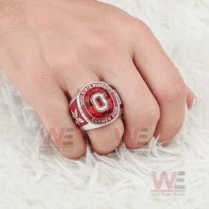 Hand wearing an Ohio State Buckeyes ring with red gemstone style center raised block O logo and Ohio State Buckeyes Carmen Ohio text shown on a soft white fur background!