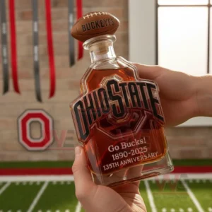 A hand holding an Ohio State glass bottle with amber liquid and football decor in the background!