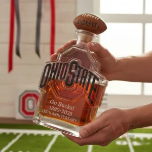 Two hands holding an Ohio State themed glass bottle with amber liquid in a sports room!