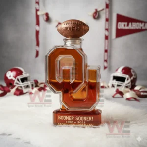 Oklahoma Sooners Boomer Sooner 1895-2025 130th Anniversary Custom Whiskey Bottle 4 A Sooners OU shaped bottle with a football cap displayed with helmets ribbons and wall décor.
