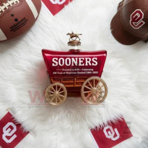 Oklahoma Sooners 130 Years Of Oklahoma Football Whiskey Bottle 7 A wagon shaped Sooners bottle lies on a fluffy white rug with team items and football gear placed around it!