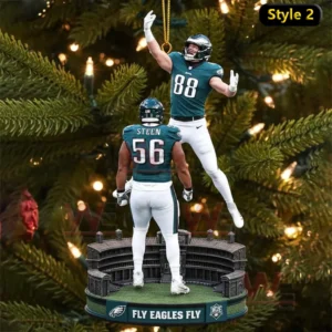 Holiday ornament hanging on a Christmas tree showing two Philadelphia Eagles players celebrating above a stadium base with text reading Fly Eagles Fly.