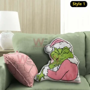 Pink grinch shaped pillow leaning on a green sofa with holiday styling next to a pink decorative cushion in a cozy living room!
