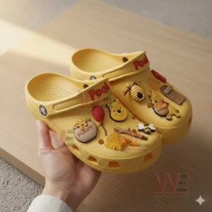 Yellow Pooh clogs held by a hand decorated with charms shaped like honey pots balloons bees honeycombs and Pooh character icons.