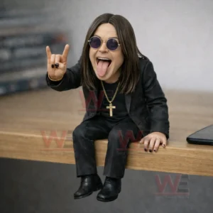 Resin figure of a long haired rock singer in a black suit and round sunglasses sitting on a desk with tongue out and making a rock hand sign!