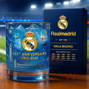 A Real Madrid anniversary glass with blue ice positioned beside a decorative gift box in a stadium setting.
