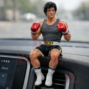 A small Rocky themed boxer figurine with red gloves sitting on a car dashboard in front of a blurred street view!