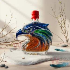 A glass eagle head bottle with red cap on white fur with branches rocks and feathers nearby.
