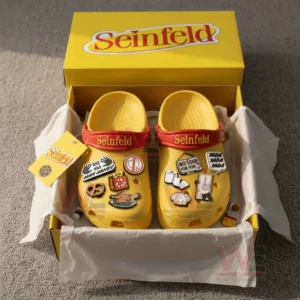 A pair of yellow themed clogs shown in an open box featuring multiple charms representing iconic comedic elements!