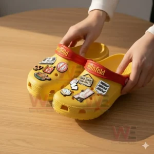 Seinfeld Crocs Crocband Clogs With Charms 4 A close view of yellow decorative clogs with comedy inspired charms touched lightly by a hand!