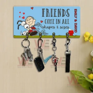 Friends come in all shapes and sizes key holder plaque with four hooks holding keys displayed on a beige wall with flowers and greenery beside it.