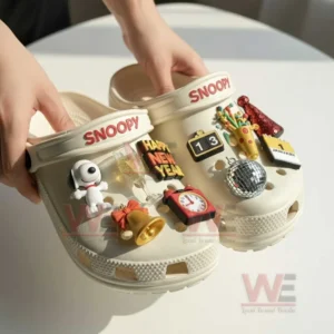 Snoopy Happy New Year Crocs Clogs with Charms 3 Pair of light colored clogs held up to display festive charms playful details and a cheerful celebration style!